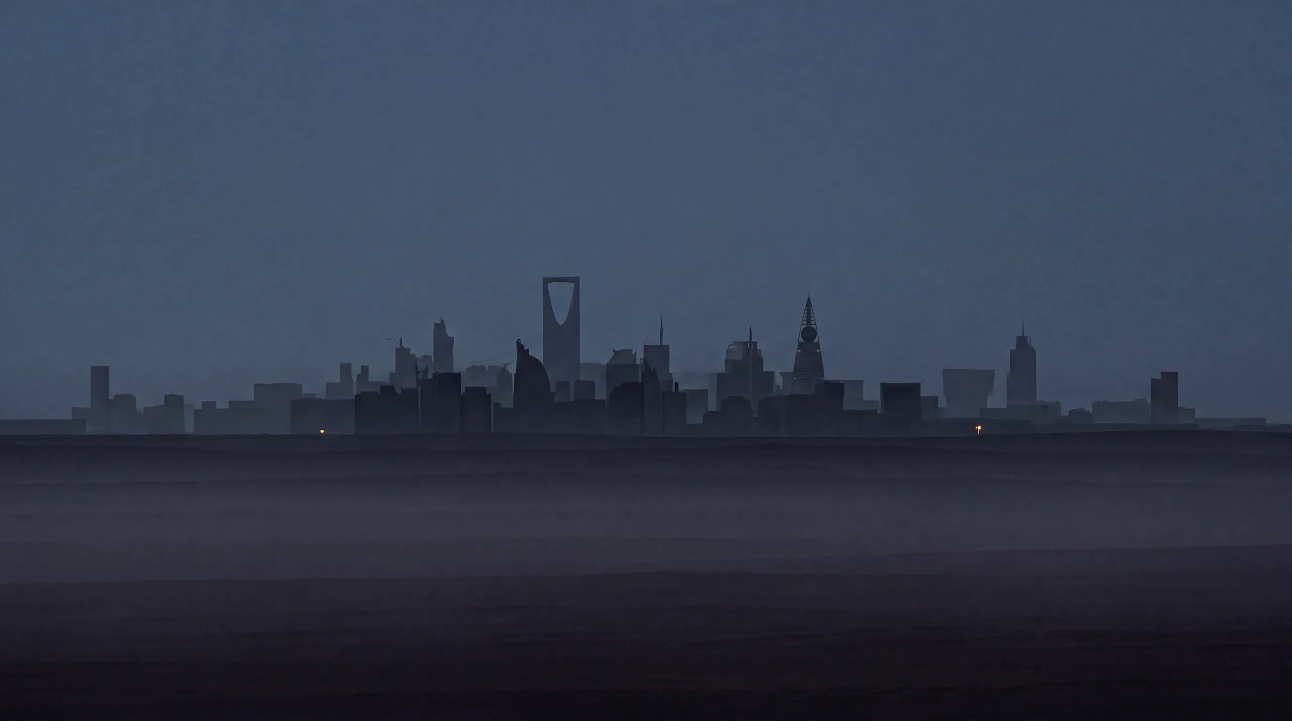 The Riyadh skyline at dusk, towers reduced to flat silhouettes in desert haze.
