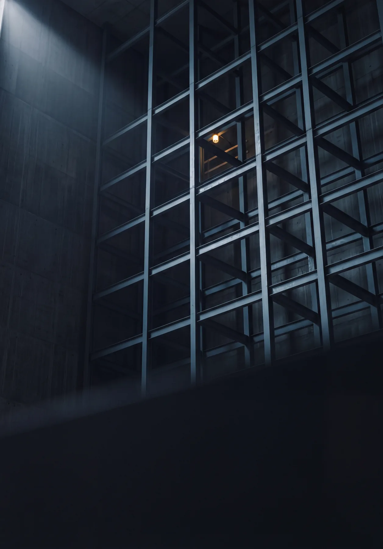 Tall empty steel racking in a concrete hall, one bulb burning high in the frame.