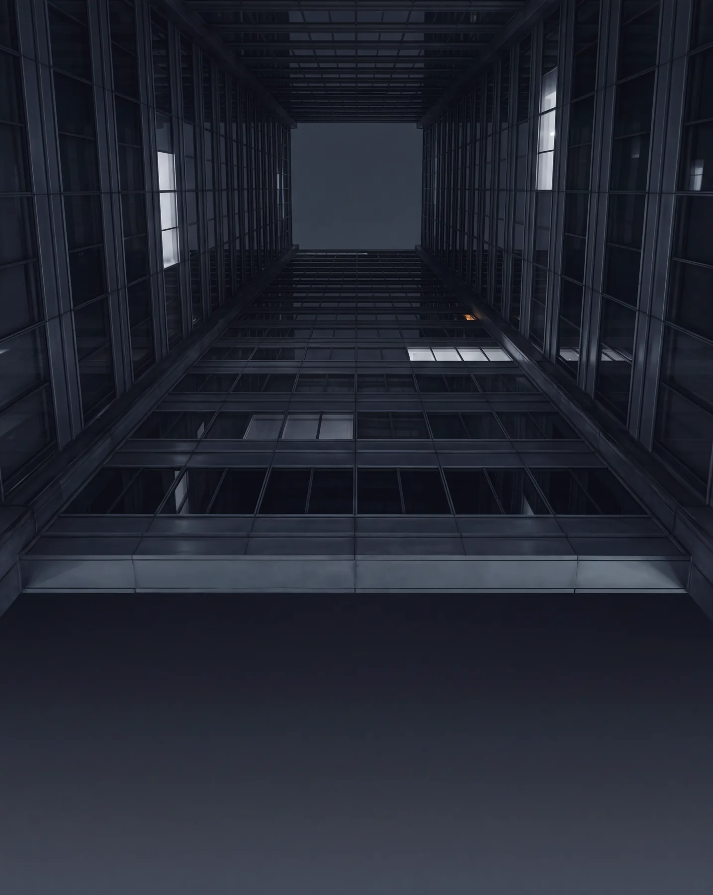 Looking up through the glass atrium of an office tower toward a pale square of sky.
