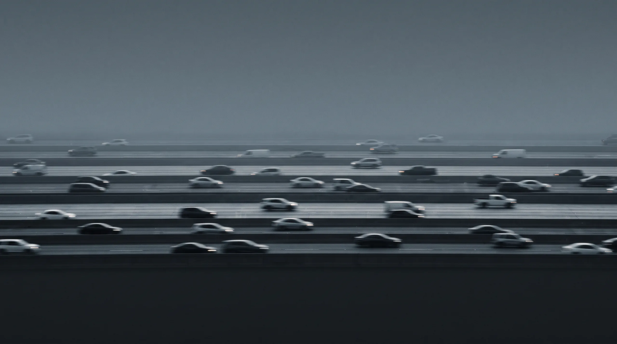 Multi-lane motorway traffic in fog, the vehicles reduced to soft parallel bands.